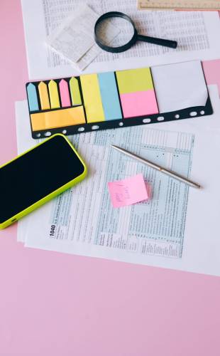 Assorted office supplies and tax forms on a vibrant pink surface with copy space.