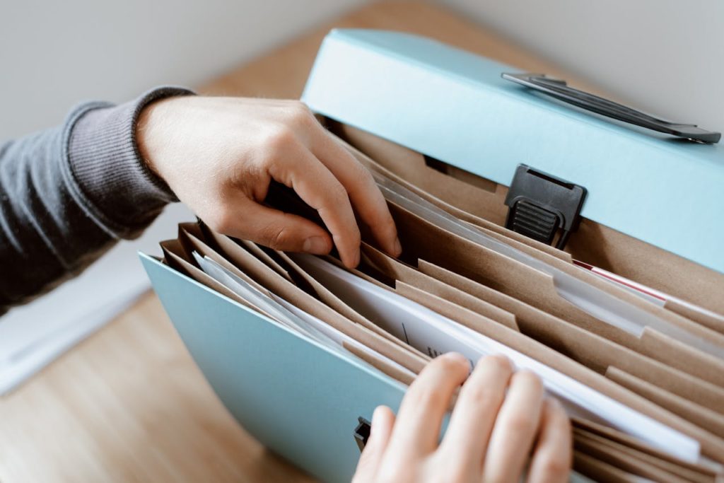 pexels photo 4792285 Close-up of hands organizing papers in a blue folder, ideal for business and office concepts.