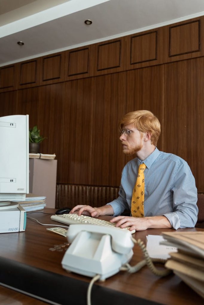 pexels photo 8872599 Businessman in vintage office setting, focused on computer work, dressed in retro attire.